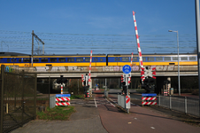 832586 Gezicht op de spoorwegovergang in de Eykmanlaan te Utrecht, met een passerende trein op het viaduct voor de hoge ...